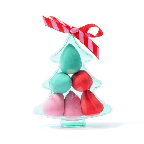 A Christmas tree-shaped clear plastic container holding six makeup sponges in pastel pink, mint green, and bright red, tied with a red-and-pink striped ribbon on a white background.